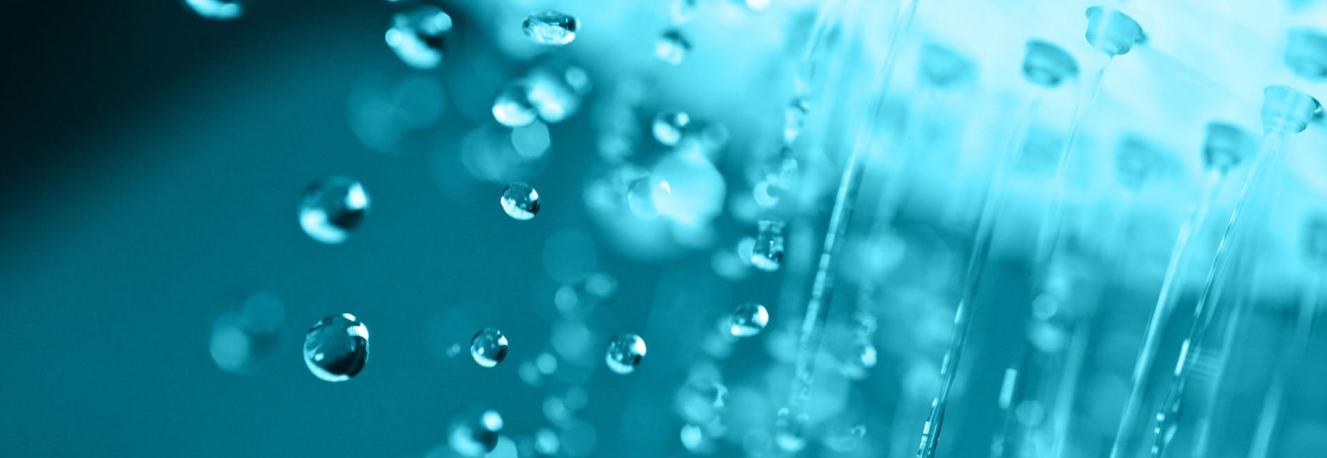 Nahaufnahme von Wasserstrahlen und Tropfen einer Dusche vor blauem Hintergrund, Symbolbild für Sanitärtechnik und Badgestaltung